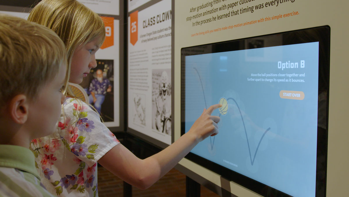 Two children at a large touchscreen, one drawing an arc across it as part of an animation timing exercise.
